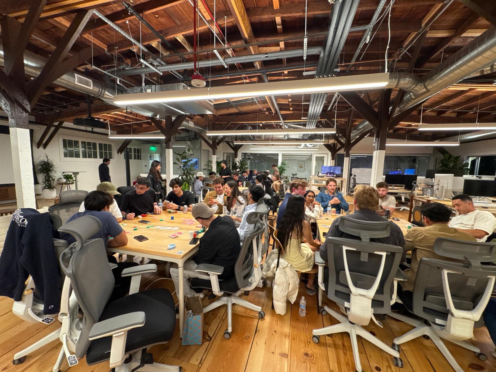 A loft office with wooden beams packed with people playing poker at long tables